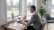 En midaldrende mand med gråt hår sidder ved et skrivebord og arbejder på en bærbar computer. På skærmen er et diagram af et varmesystem. Ved siden af computeren ligger nogle papirer og en smart home-enhed